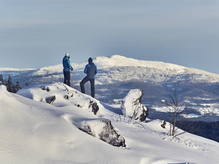 Zwei Wanderer mit Stöcken auf verschneitem Berg mit Blick auf schneebedeckte Landschaft