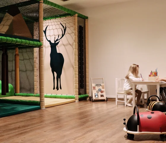Kinder spielen an einem Tisch neben einem Klettergerüst mit Hirsch-Silhouette