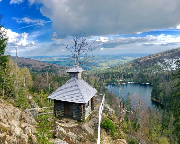 Kleine Holzhütte auf Felsen mit Blick auf bewaldeten See und Berge