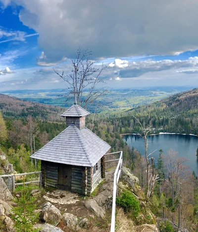 Kleine Holzhütte auf Felsen mit Blick auf bewaldeten See und Berge