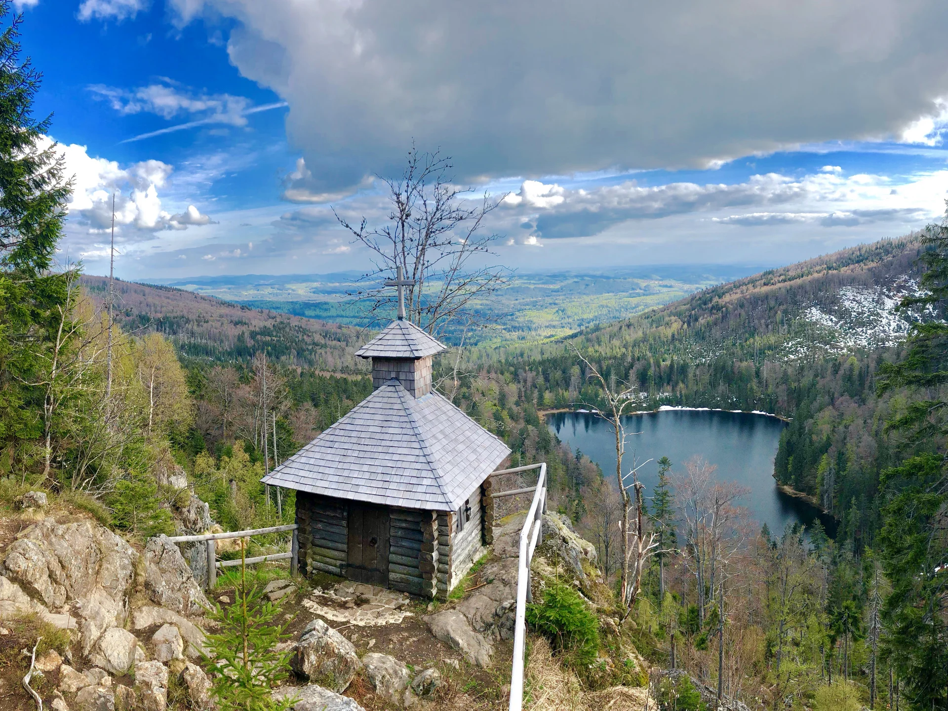 Kleine Holzhütte auf Felsen mit Blick auf bewaldeten See und Berge