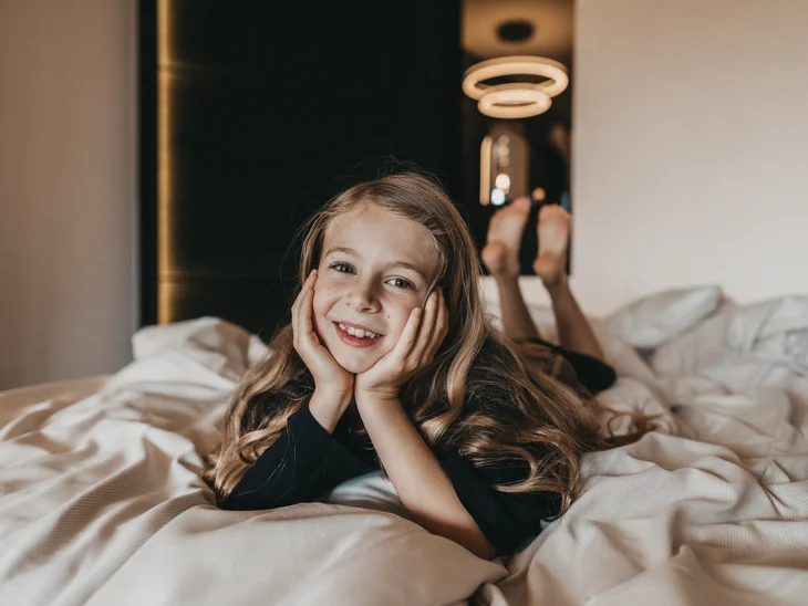 Lächelndes Mädchen liegt auf einem Bett in einem modernen Hotelzimmer