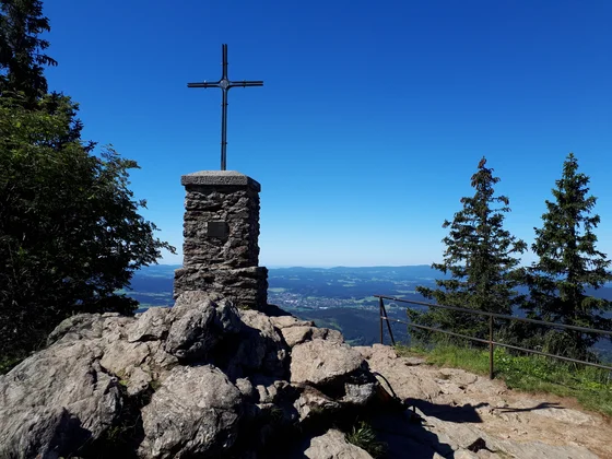 Steinkreuz auf Berggipfel mit Blick auf Tal und blauen Himmel