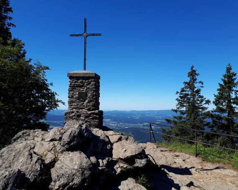 Steinkreuz auf Berggipfel mit Blick auf Tal und blauen Himmel