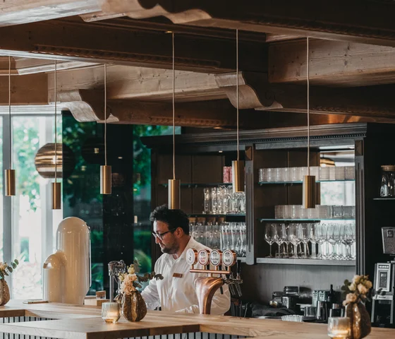 Mann hinter einer Bar mit Holzdecke und modernen Pendelleuchten