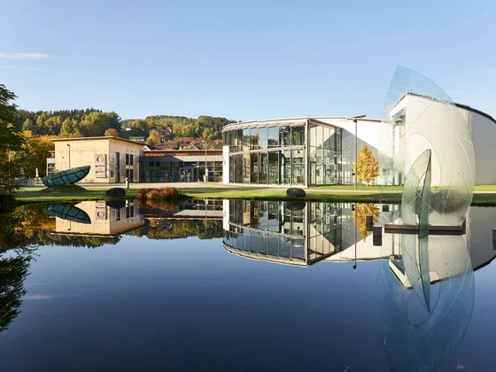 Modernes Gebäude mit Glasfassade und Skulptur am ruhigen Teich