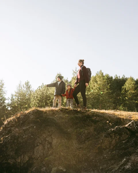 Woman with two children hiking on a sunny hill with a forest in the background