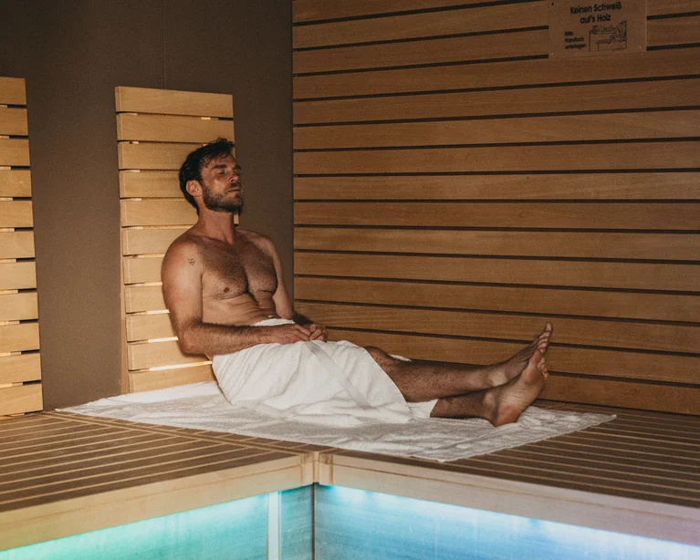 Man relaxing in sauna sitting on wooden benches with towel around waist