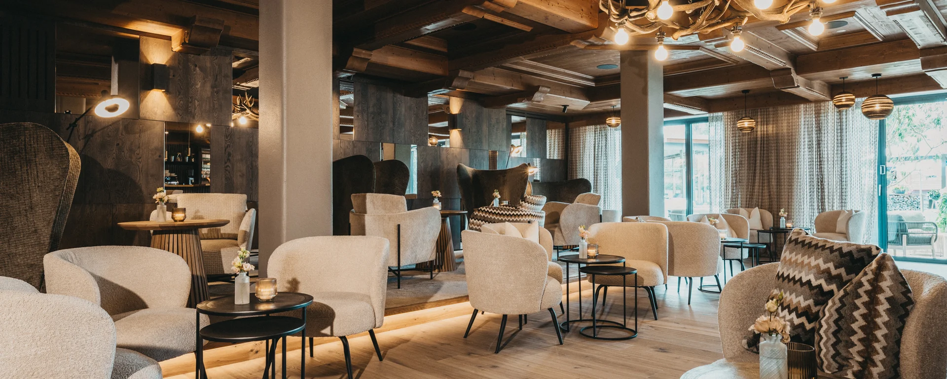 Gemütliche Lounge mit beigen Sesseln, Holzboden und Hirschgeweih-Lampe