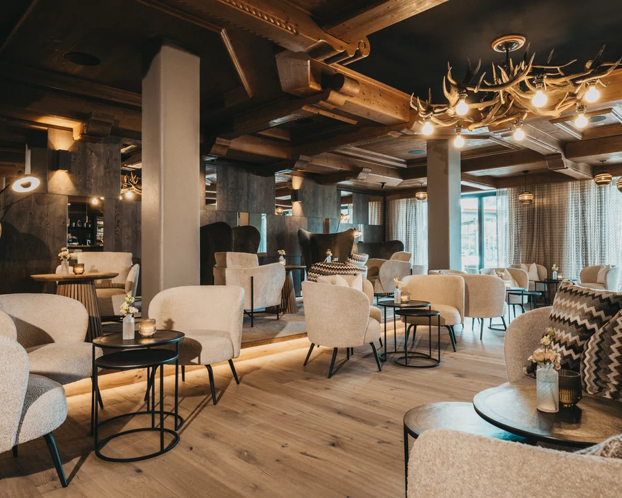 Gemütliche Lounge mit beigen Sesseln, Holzboden und Hirschgeweih-Lampe