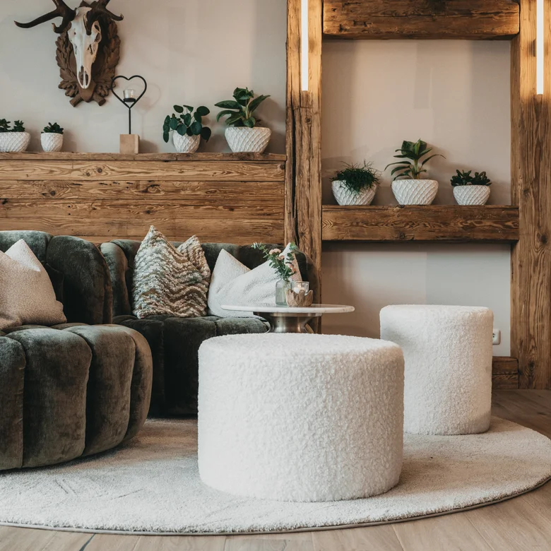 Gemütliche Sitzecke mit grünem Sofa, weißen Hockern und Holzdekor