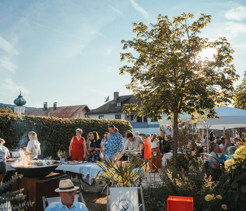 Menschen bei einer Gartenparty mit Grill und Sonnenschirm an einem sonnigen Tag
