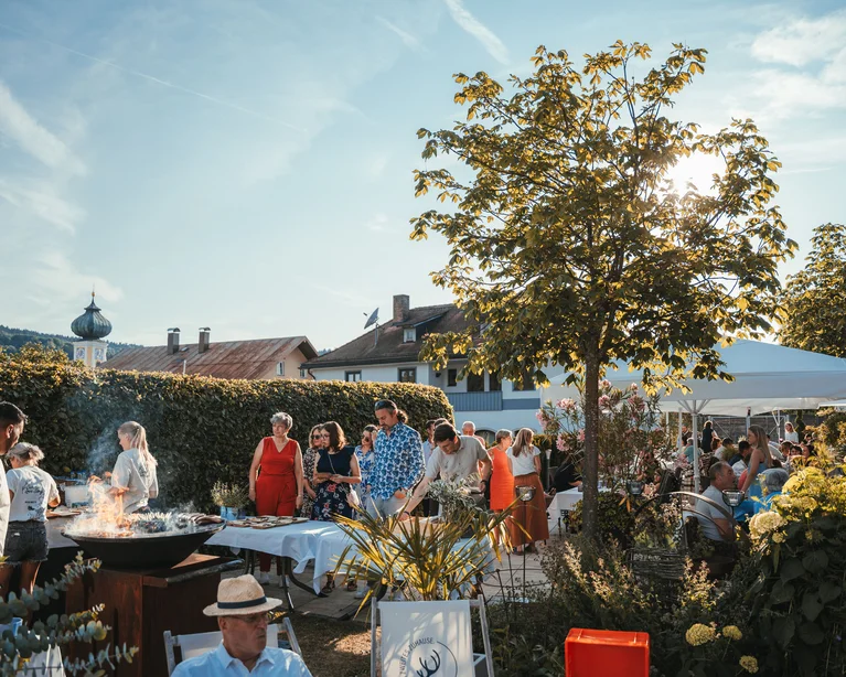 Menschen bei einer Gartenparty mit Grill und Sonnenschirm an einem sonnigen Tag