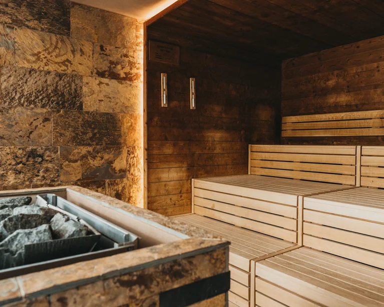 Innenansicht einer Sauna mit Holzbänken und Steinofen