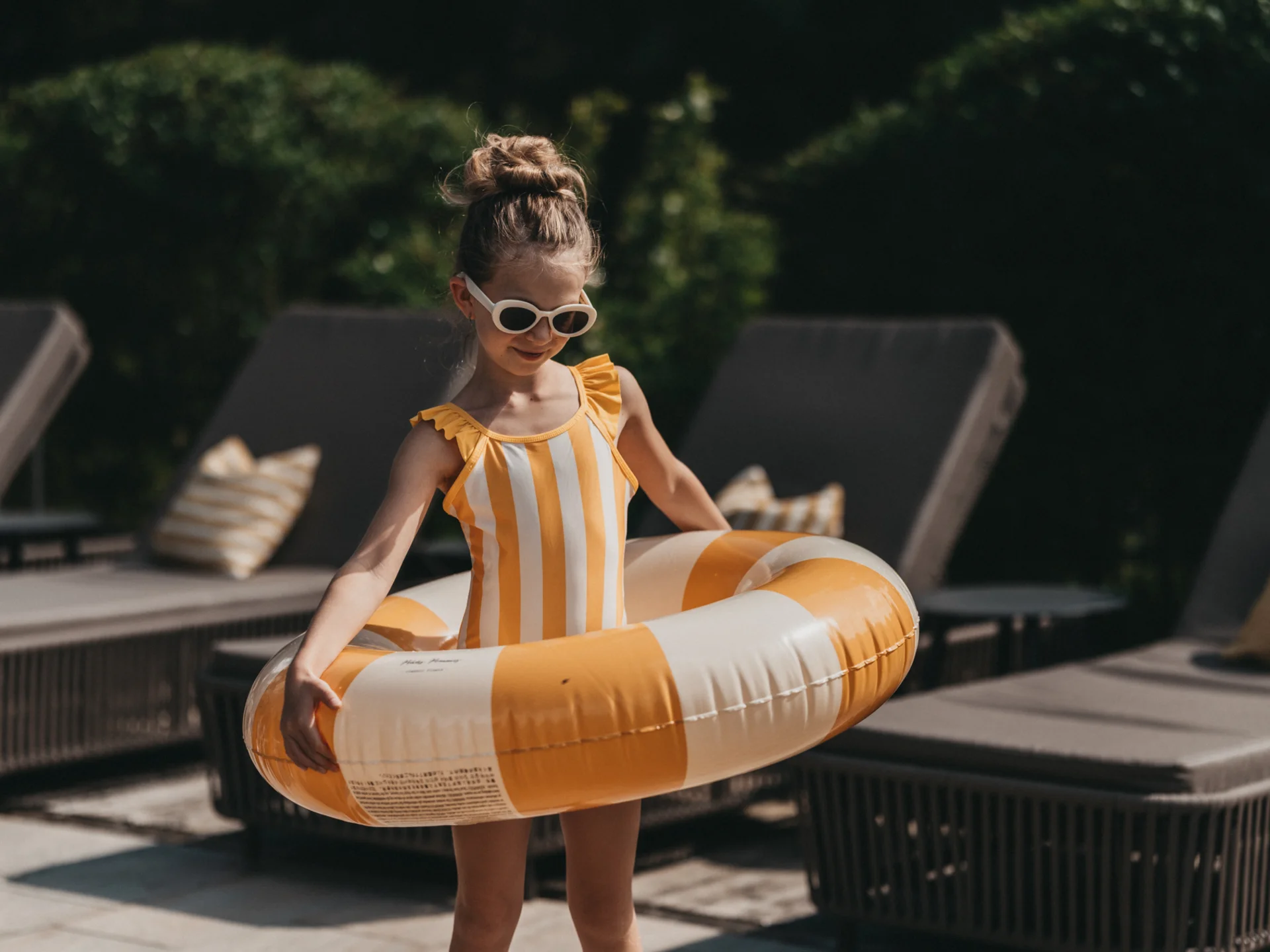 Mädchen mit Sonnenbrille und gestreiftem Badeanzug hält Schwimmreifen am Pool