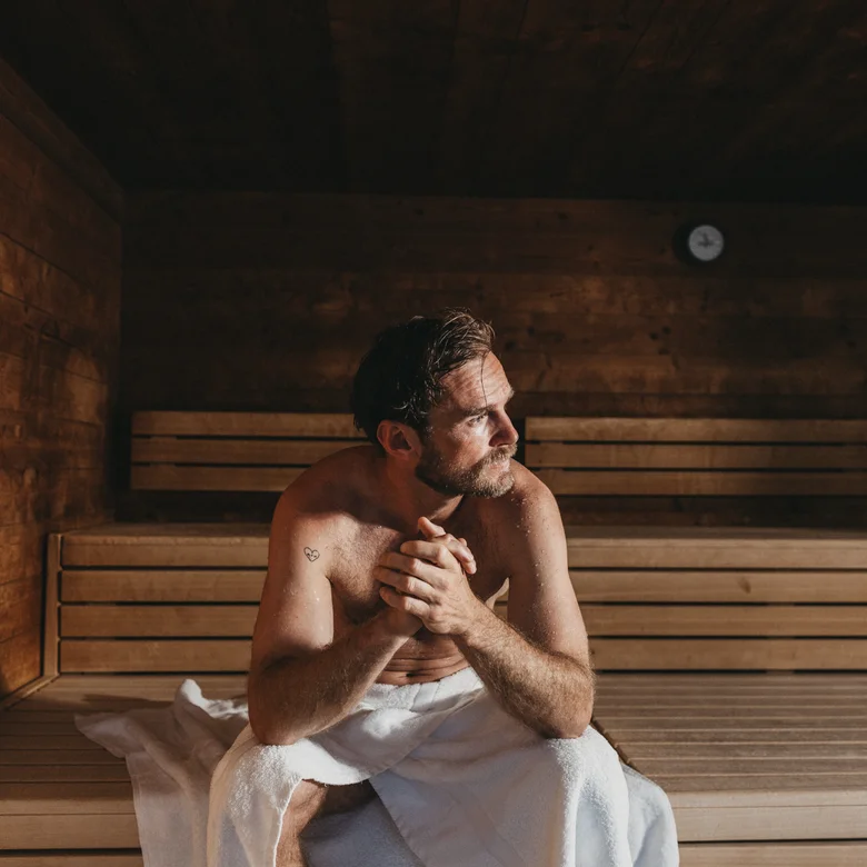 Mann mit Handtuch sitzt nachdenklich in einer Holzsauna
