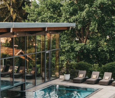 Moderner Poolbereich mit Liegestühlen und Glasgebäude umgeben von Bäumen