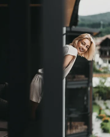 Frau lehnt lächelnd über Balkonbrüstung mit Blick auf Garten und Berge