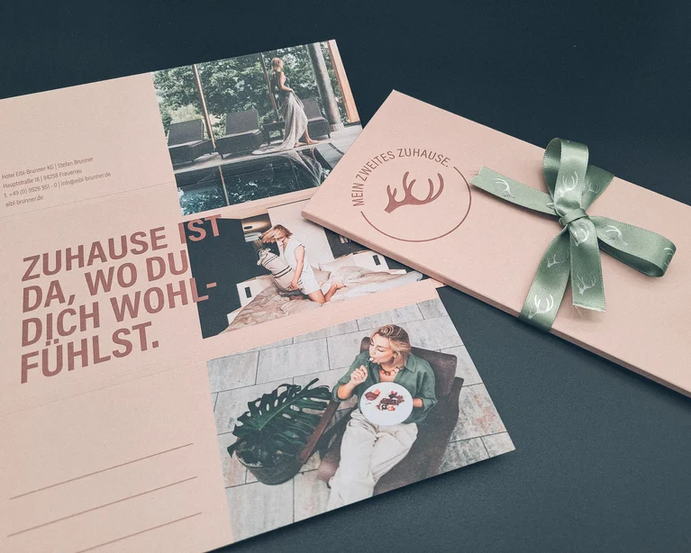 Hotelbroschüren und Geschenkbox mit grünem Band auf dunklem Hintergrund