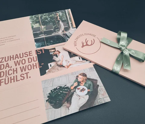 Hotelbroschüren und Geschenkbox mit grünem Band auf dunklem Hintergrund