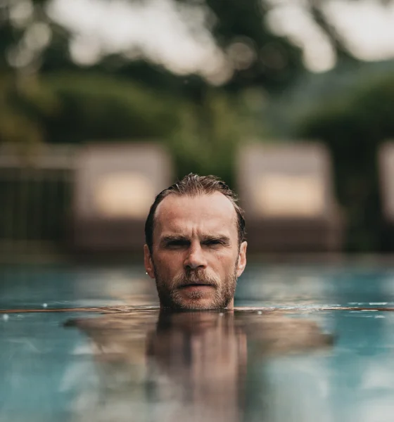 Mann entspannt im Pool mit Liegestühlen und Pflanzen im Hintergrund
