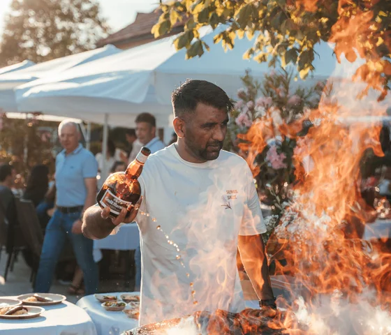 Mann gießt Flüssigkeit auf Grill mit großen Flammen bei Outdoor-Event