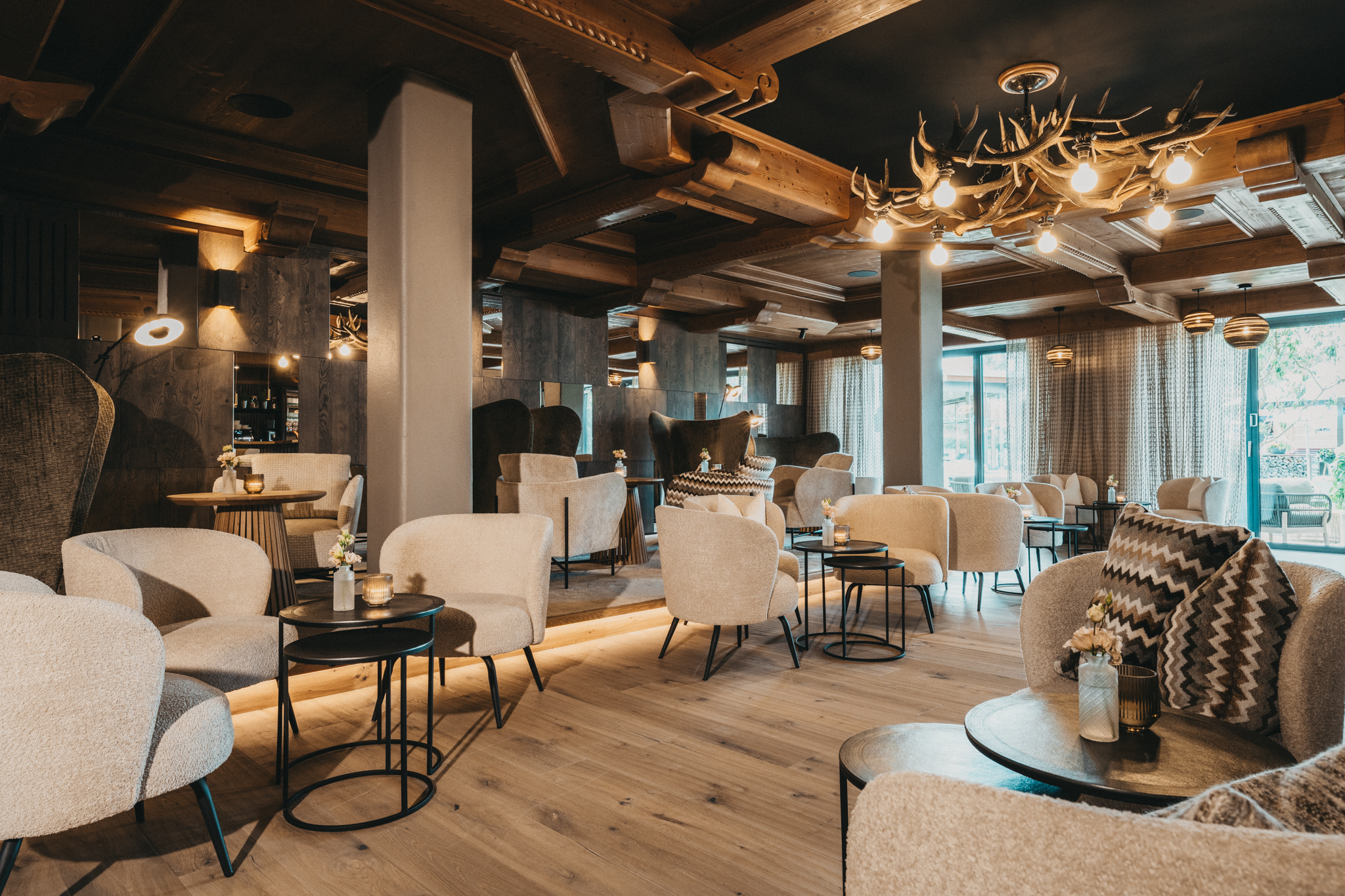 Gemütliche Lounge mit beigen Sesseln, Holzboden und Hirschgeweih-Lampe